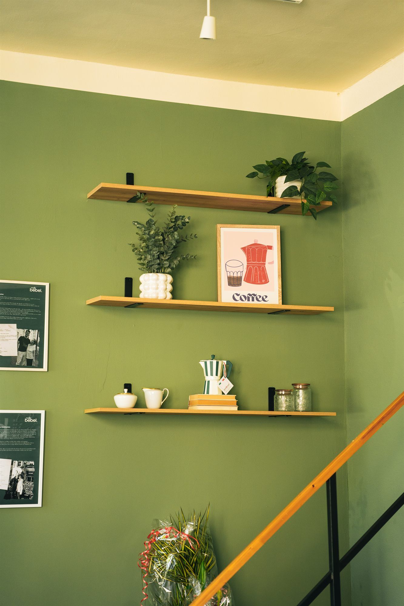 Regal mit Kaffee-Utensilien, Pflanzen und Schürze an der grünen Wand im Café Bebel